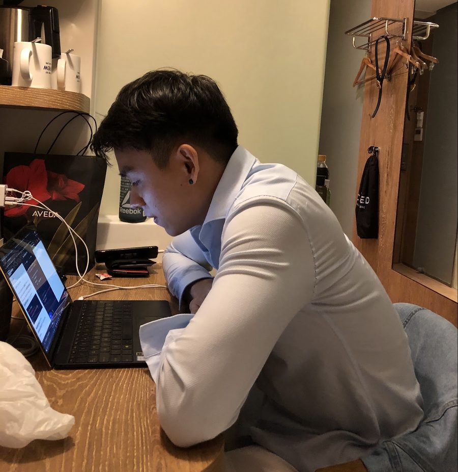 Deric hunched over a laptop coding in a hotel room in Singapore, 2019