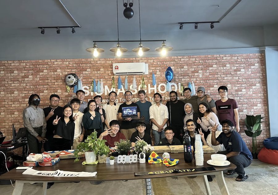 Sigmaschool August 2024 batch graduation, the whole group behind a table of pizza and GRADUATE sashes